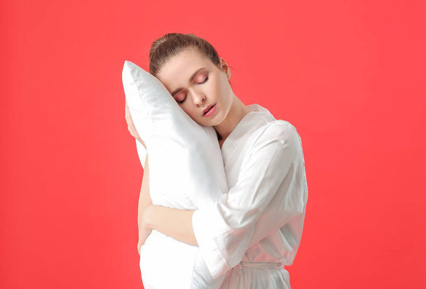 Tired woman with pillow on color background. Concept of sleep deprivation - Foto, afbeelding