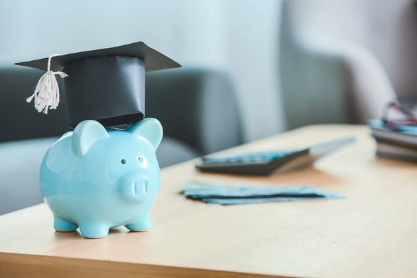 Piggy bank met graduatie cap op tafel in de kamer - Foto, afbeelding