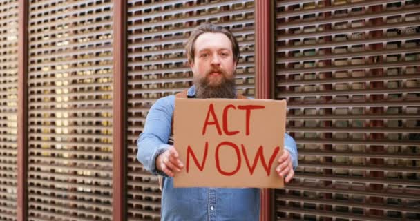 Retrato de tiro do jovem caucasiano demonstrando cartaz com palavras Act Now. Ativista do sexo masculino mostrando quadro com protesto sobre questões políticas ou ambientais. Protesto solitário. Conceito de ativismo
. - Filmagem, Vídeo
