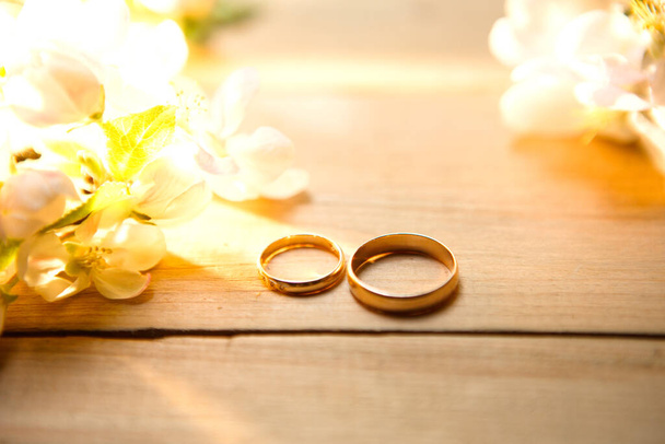 Two gold rings on a wooden background with white Apple blossoms. Wedding in eco-style, rustic. Couple in love, ceremony and registration, details, bride's fees, groom's morning. Space for text. flatly. - Foto, immagini