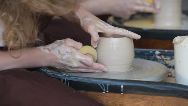 Jonge pottenbakker in schort op het werk. Ambachtelijke kunstenaar vormt de kruik met haar handen en een speciaal gereedschap op aardewerk wiel. - Video