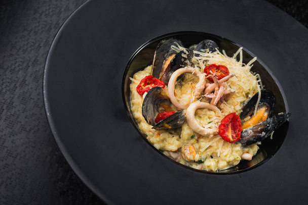 risotto with seafood, mussel and squid and italian cheese in black dish. restaurant serving meals - Photo, Image