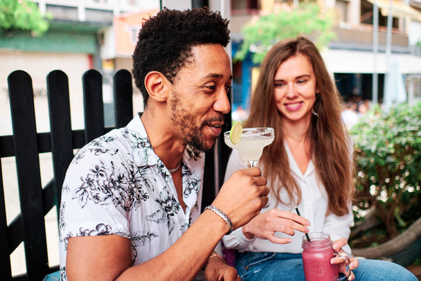 夏にバーでカクテルを飲むのが好きな若い異人種間のカップル - 写真・画像