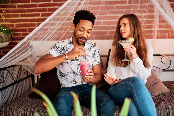 Ein verliebtes interrassisches Paar trinkt einen Cocktail in einer exklusiven Bar - Foto, Bild