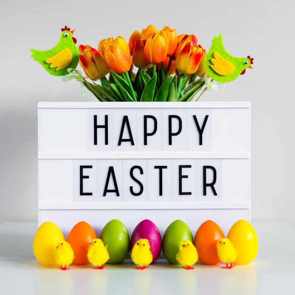 Primer plano de la caja de luz vintage con felices saludos de Pascua, flores, huevos coloridos y pollitos decorativos en la mesa
 - Foto, imagen