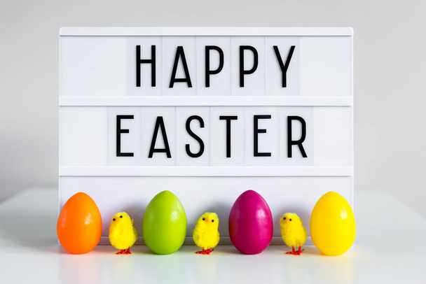 close up of vintage lightbox with happy Easter greetings, colorful eggs and decorative chicks on the table - Foto, Imagem