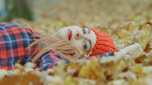 Portret pięknej kobiety w czerwonym kapeluszu leżącej w żółtych jesiennych liściach. Kobieta model korzystających z życia na zewnątrz natura tło 4k zwolnione tempo - Materiał filmowy, wideo