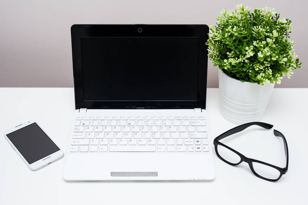 自宅やオフィスの職場-テーブルの上の鍋に空白の画面、眼鏡や植物とノートパソコンやスマートフォン - 写真・画像