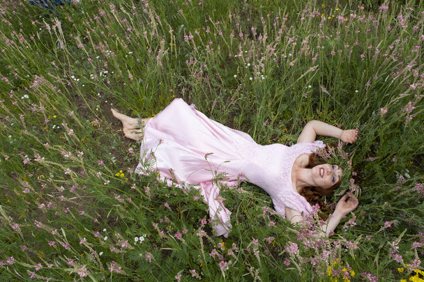 dívka v dlouhých růžových šatech leží na poli mezi kvetoucí alfalfa - Fotografie, Obrázek