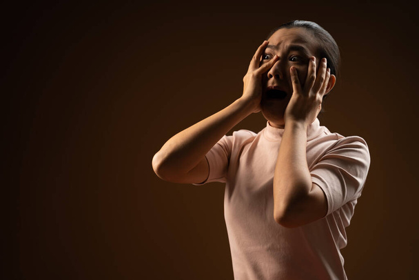 Asian woman scared screaming covering face by her hands standing isolated on beige background. Low key. - Photo, Image