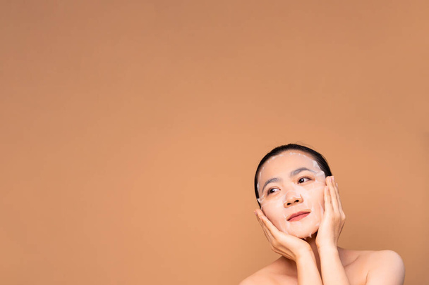 Portrait of Asian woman with facial mask standing isolated on beige background. Cosmetic Beauty spa. - Foto, afbeelding