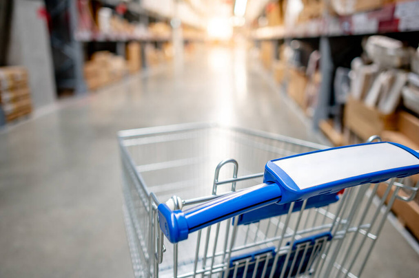 Empty shopping cart or shopping trolley in aisle of supermarket or grocery store. Buying concept - Photo, Image