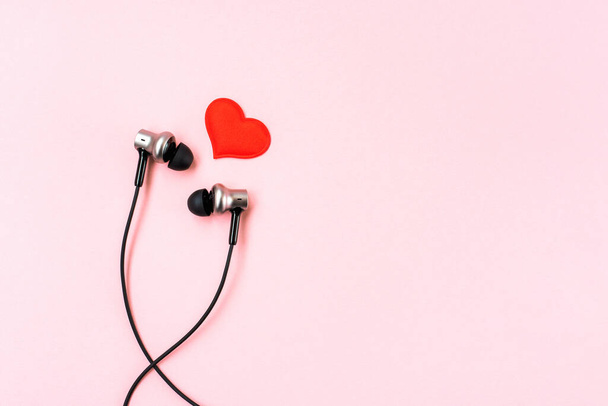 Červené srdce s černými hudebními sluchátky pro smartphone na růžové pastelové pozadí. Romantický a milostný koncept. Krásná dárková pohlednice. Minimalistický byt. Prázdné místo pro psaní. Rozumím. Horní pohled.  - Fotografie, Obrázek