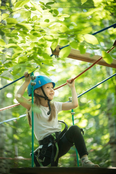 Екстремальні пригоди мотузки в лісі маленька дівчинка стоїть на мотузковому мосту і посміхається дивлячись вгору
 - Фото, зображення