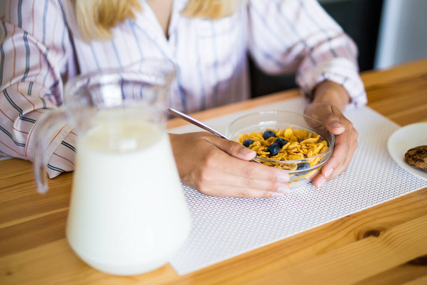 healthy breakfast concept - close up of corn flakes with blueberry in glass bowl and female hands - Photo, Image