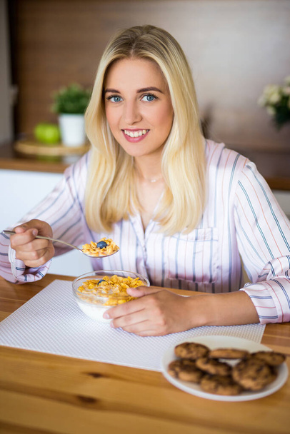 healthy breakfast - young cheerful woman eating corn flakes with milk in modern kitchen - Фото, изображение