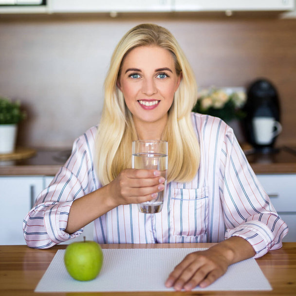 bella ragazza con mela e bicchiere d'acqua in cucina moderna - Foto, immagini