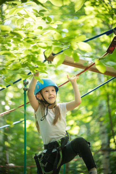 Aventura de cuerda en el bosque - niña sonriente parada en el puente de cuerda - mirando hacia arriba
 - Foto, Imagen