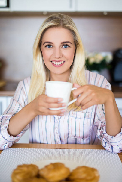 desayuno joven mujer en pijama beber café con pastelería en la cocina
 - Foto, Imagen