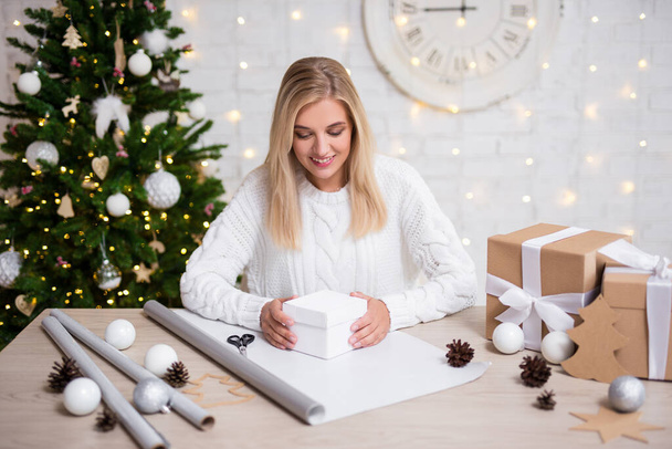 junge schöne Frau verpackt Weihnachtsgeschenke in dekoriertem Wohnzimmer - Foto, Bild