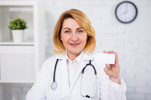 retrato de mulher madura alegre médico mostrando seu cartão de visita
 - Foto, Imagem