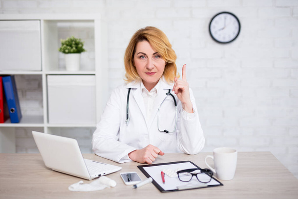 potrtait of serious mature female doctor showing attention sign in modern office - Photo, Image