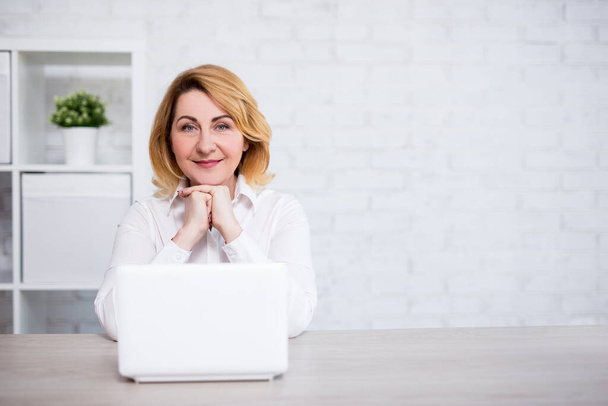 donna matura seduta con computer portatile in ufficio moderno o in soggiorno - copiare spazio su parete di mattoni bianchi - Foto, immagini
