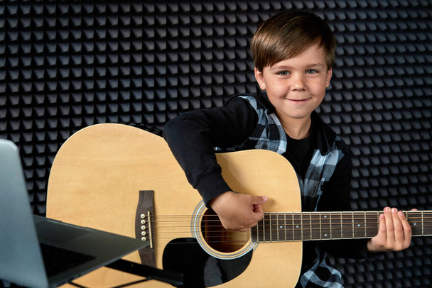 Smiling brunette boy is playing the guitar. Learn to play a musical instrument. - Fotografie, Obrázek