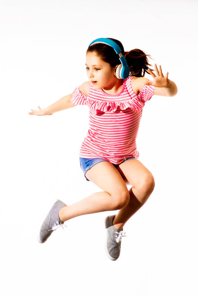 Little jumping caucasian girl with a headphones on white background - Foto, imagen
