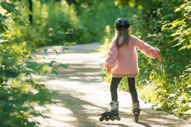 Маленька дівчинка в рожевому светрі катається в лісі на роликах
 - Фото, зображення