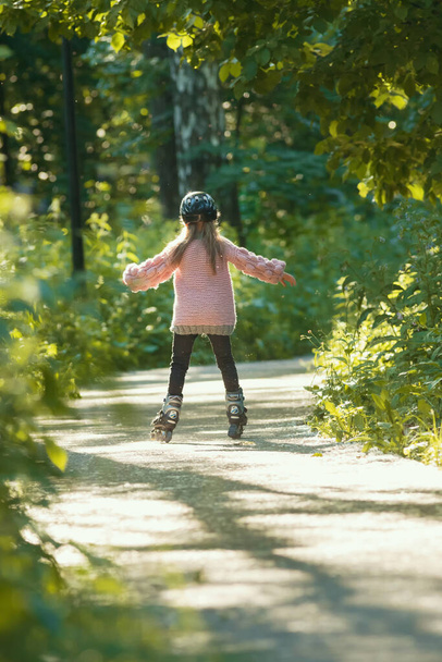 Маленька дівчинка в рожевому светрі катається в парку на роликах
 - Фото, зображення