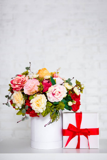 bouquet estivo di bei fiori e scatola regalo sul tavolo su sfondo muro di mattoni bianchi con spazio copia - Foto, immagini