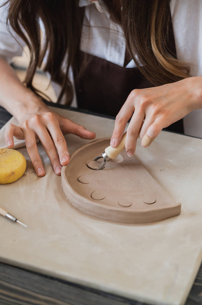 Kobieta pracująca z gliny z rękami i pętli narzędzia cięcia zbliżyć w warsztacie garncarskim. - Zdjęcie, obraz