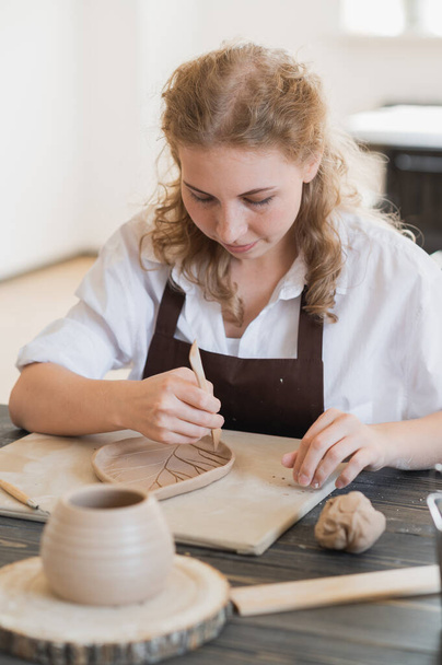 Женские руки держат палку и делают орнамент на декоративном продукте. глина мастер формования глины на керамической мастерской. - Фото, изображение