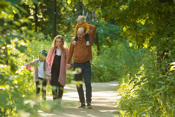 Молодая счастливая семья родителей с двумя маленькими детьми гуляет в парке
 - Фото, изображение