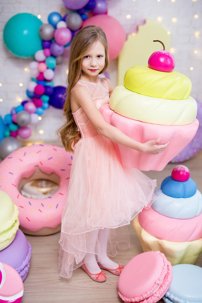 портрет милої маленької дівчинки, що позує з великим кексом і штучним гігантським тістечком
 - Фото, зображення