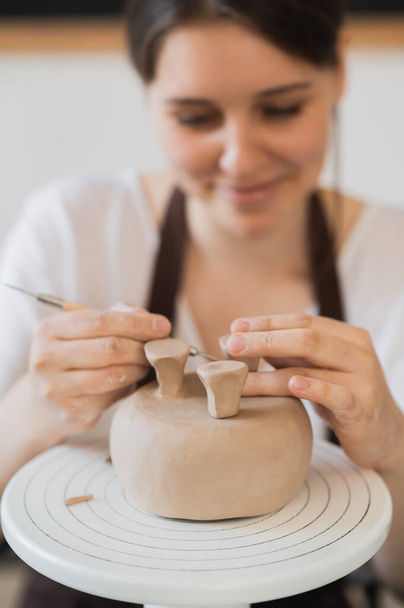 Close-up van vrouwelijke pottenbakker holding stick en het maken van ornament op aardewerk. Klei meester gieten klei product. Concept van keramische kunst en hobby. - Foto, afbeelding