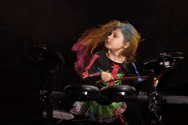 Kleine blanke meisje drummer met veelkleurig haar spelen van de elektronische drum kit, portret op zwarte achtergrond. - Foto, afbeelding