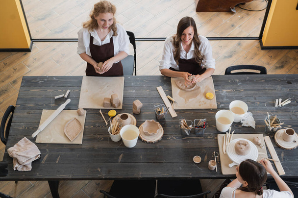 Töpferinnen während des Arbeitsprozesses in der Tonwerkstatt. Meisterinnen bereiten am großen Holztisch Keramik und Ton zu - Foto, Bild
