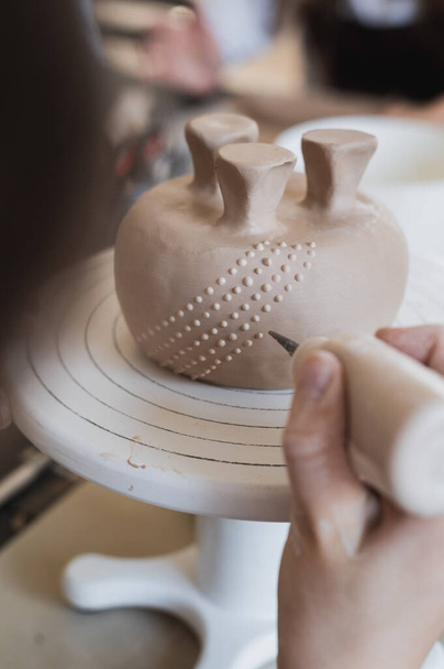 Detailní záběr na dno hrnku, který je zdoben v keramickém studiu. Ženské profesionální ruce dělat jílové tečky nebo kapky na povrchu vázy speciálním mačkacím nástrojem. - Fotografie, Obrázek
