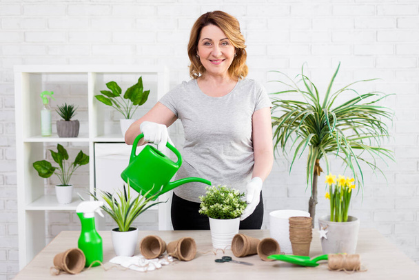 spring concept - portrait of smiling mature woman watering potted plants at home - Photo, Image