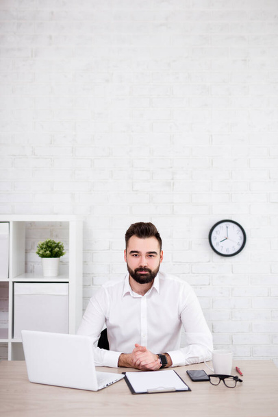 handsome bearded businessman sitting in office - copy space over white brick wall background - Photo, Image