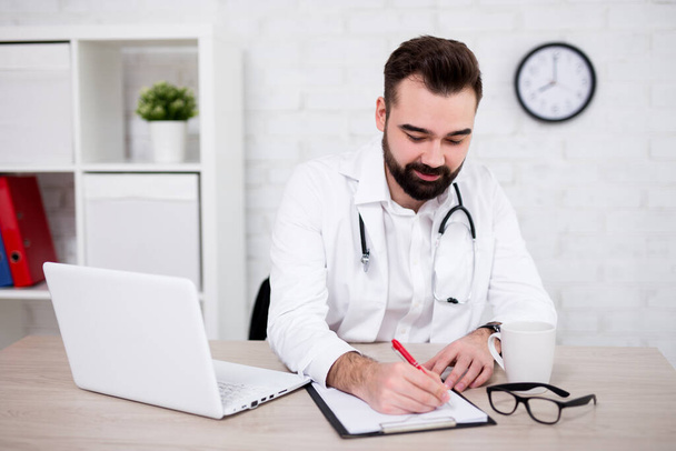 young handsome man doctor doing paperwork in office - Photo, image