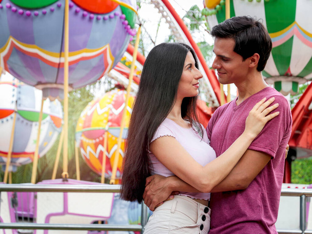 Teenager sweet couple show love each other, young beautiful woman puts her arms around boyfriend's neck, lover hug each other, spend time together at theme park, lover hang out at amusement park  - Photo, Image