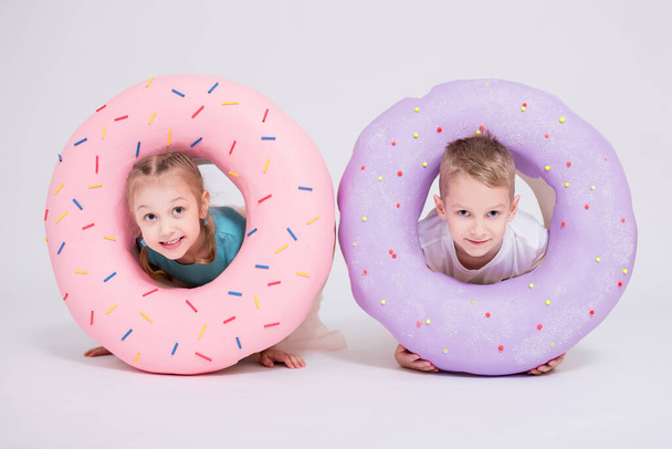cute little girl and boy with huge donuts over white background - 写真・画像