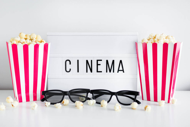 Sinema konsepti - patlamış mısırlı kırmızı çizgili kutular, 3 boyutlu gözlük ve sinema kelimeli ışık kutusu - Fotoğraf, Görsel