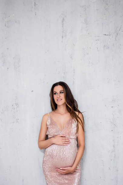 portrait of beautiful pregnant woman in shiny evening dress posing over gray wall background with copy space - Fotografie, Obrázek