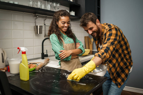 gelukkig multi-etnische paar is het schoonmaken van hun keuken en het hebben van plezier. - Foto, afbeelding