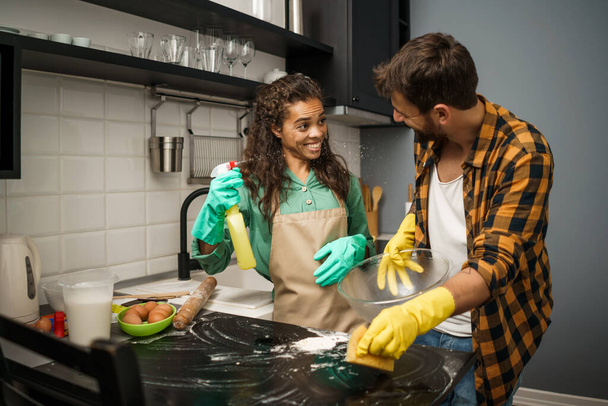 Glückliches multiethnisches Paar putzt seine Küche und hat Spaß. - Foto, Bild