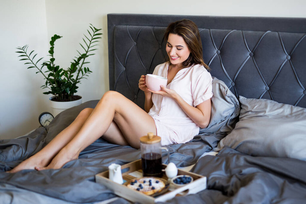 śniadanie w łóżku - młoda piękna seksowna kobieta w piżamie pijąca kawę w sypialni - Zdjęcie, obraz